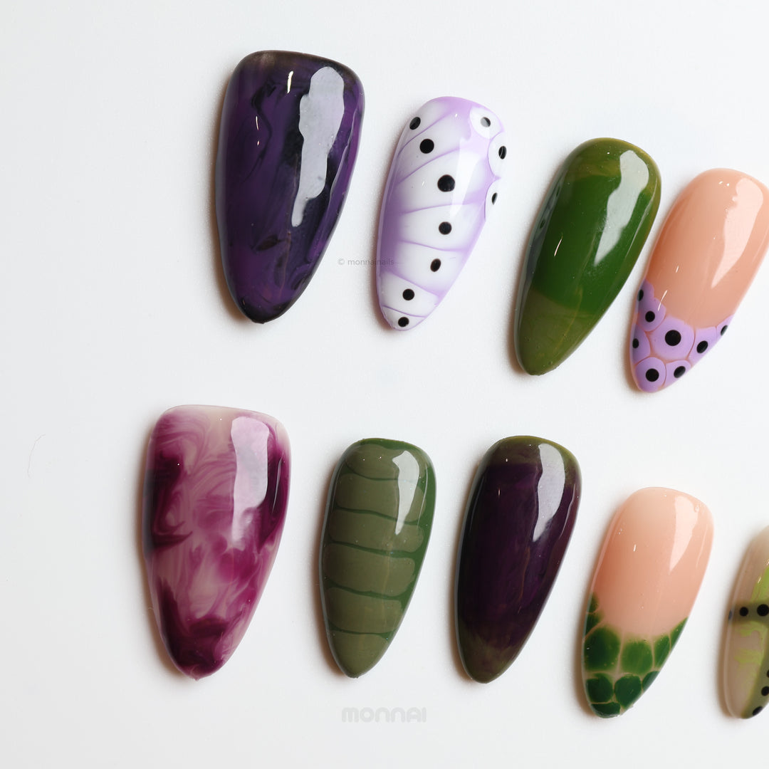 Violet Vines press-on nails laid out with glossy purple, olive green and nude moody, playful textures