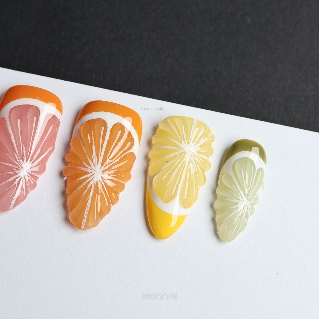 Vitamin C Crew press-on nails laid out with citrus slice designs in pink, orange, yellow, and green, glossy and raised