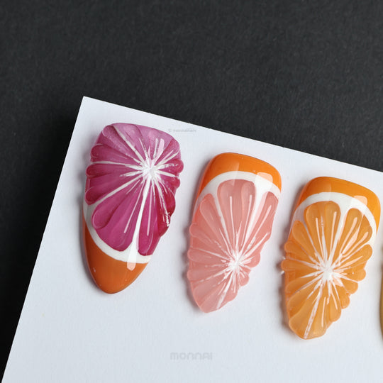Vitamin C Crew press-on nails laid out with glossy grapefruit, orange, and pink citrus slice designs