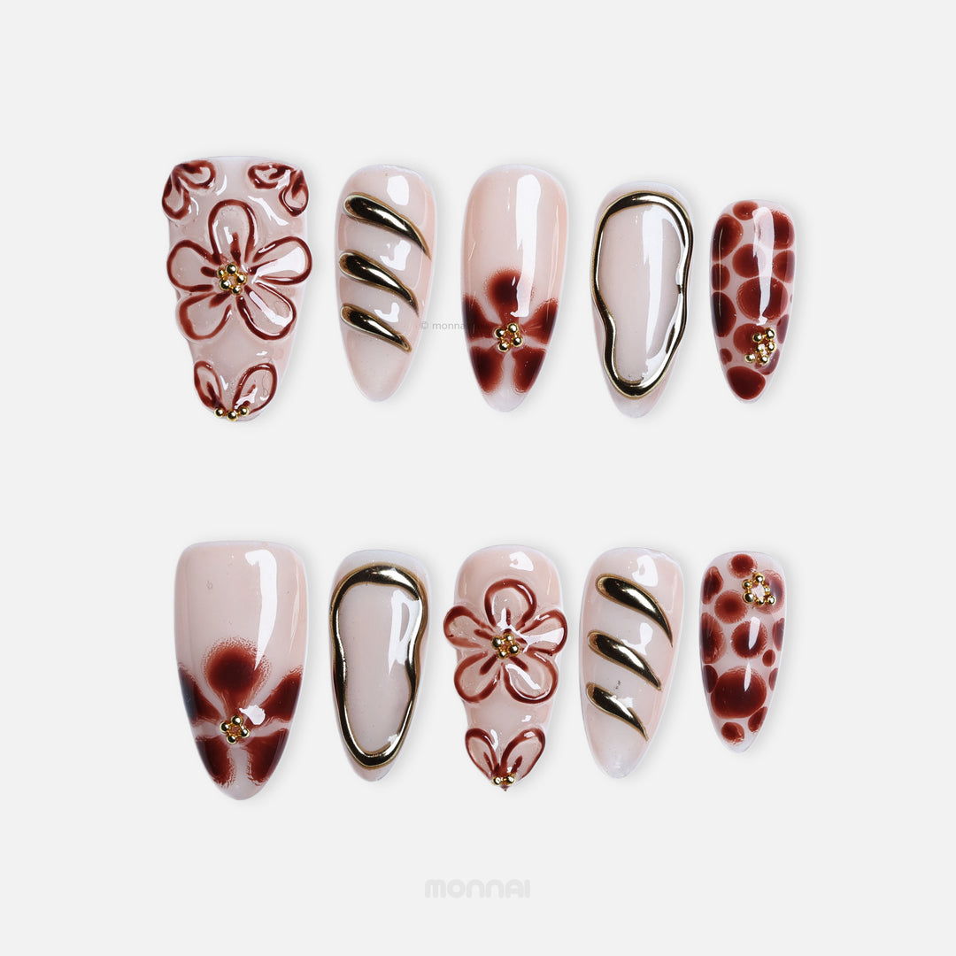 Warm Floral Glam press-on nails laid out in close-up, sheer nude with deep red florals, gold outlining, and dotted accents