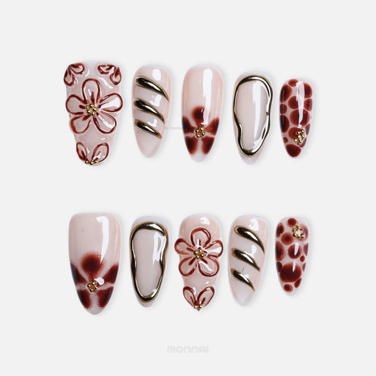 Warm Floral Glam press-on nails laid out in close-up, sheer nude with deep red florals, gold outlining, and dotted accents