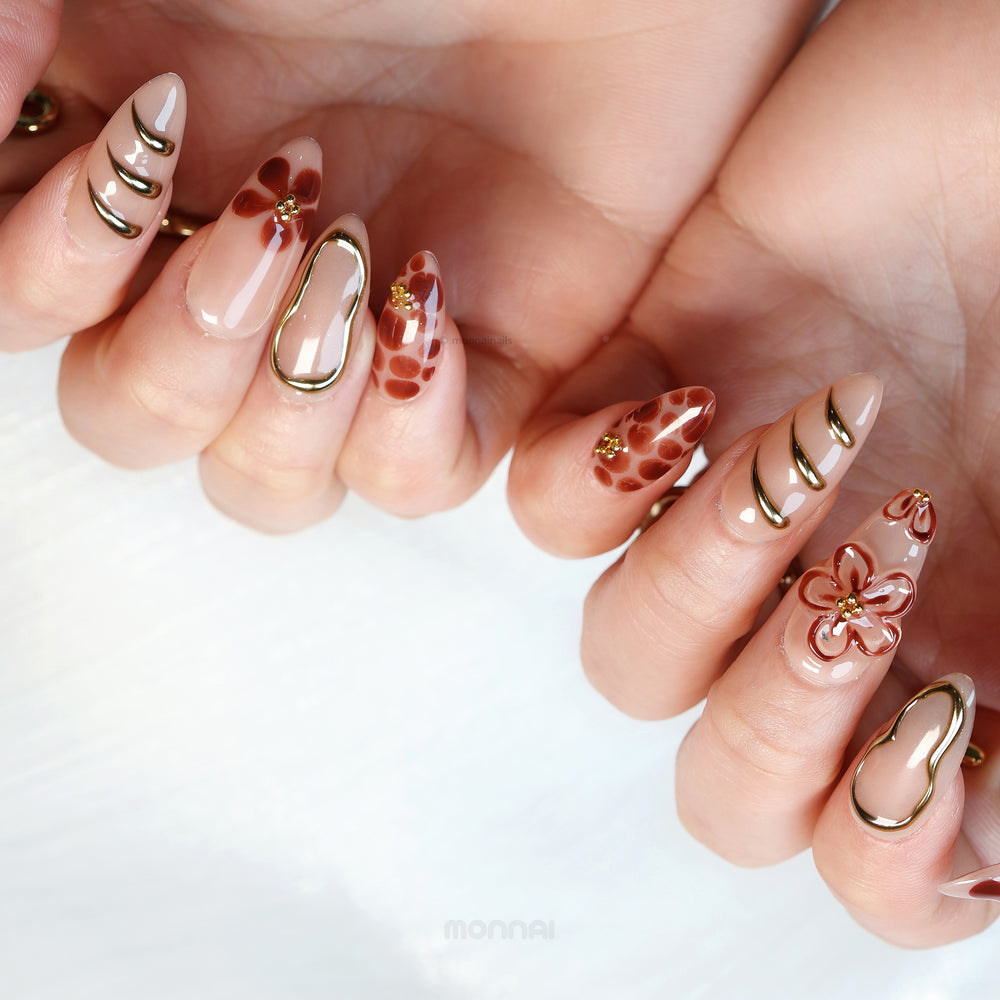 Warm Floral Glam press-on nails worn on hands with nude bases, deep red florals, and gold outlining.