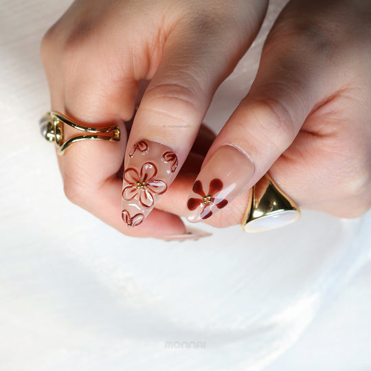 Warm Floral Glam press-on nails on hand, sheer nude with deep red floral accents and gold detailing.