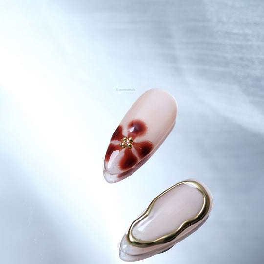 Warm Floral Glam press-on nails laid out, showing nude gloss, deep red floral detail, and gold bead accents.