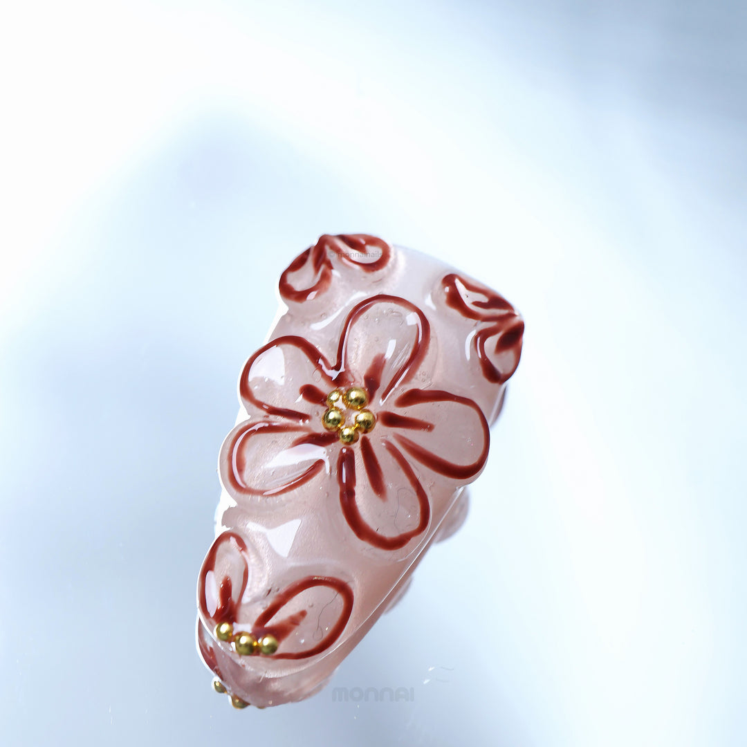 Warm Floral Glam press-on nails close-up with sheer nude base, deep red floral outlines, and gold bead accents