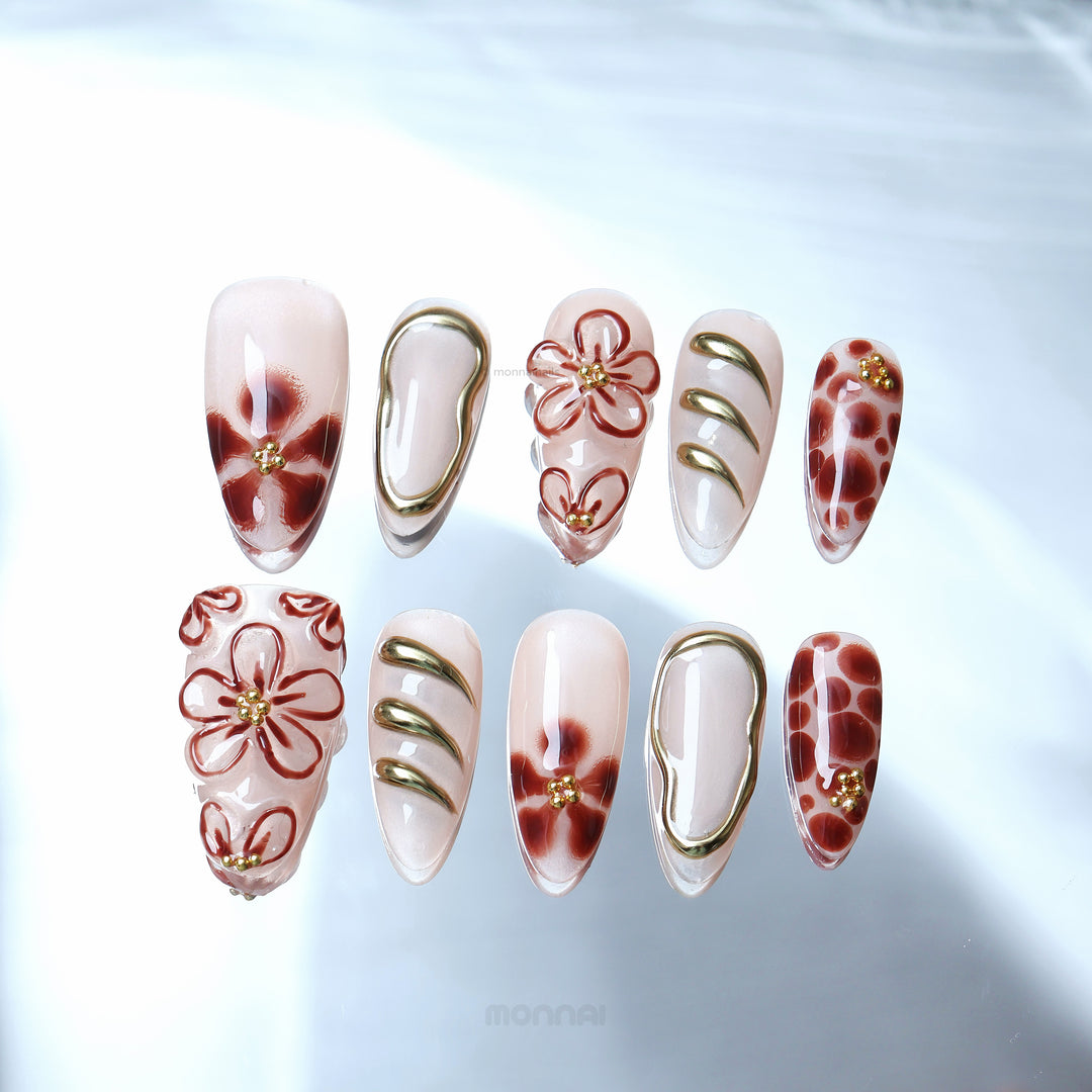 Warm Floral Glam press-on nails laid out with sheer nude base, deep red florals, dotted accents, and gold outlining