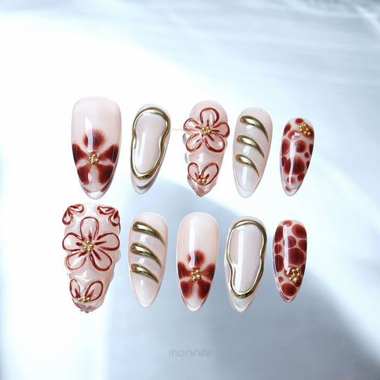 Warm Floral Glam press-on nails laid out with sheer nude base, deep red florals, dotted accents, and gold outlining