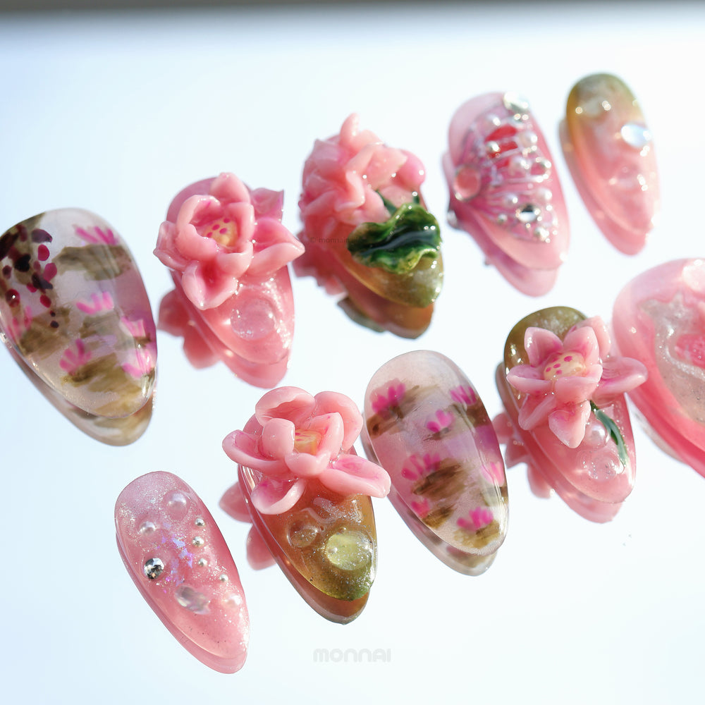 Water Lily Dream press-on nails shown laid out, with hand-painted pink floral details, sculpted water lily accents, and glossy shimmer.