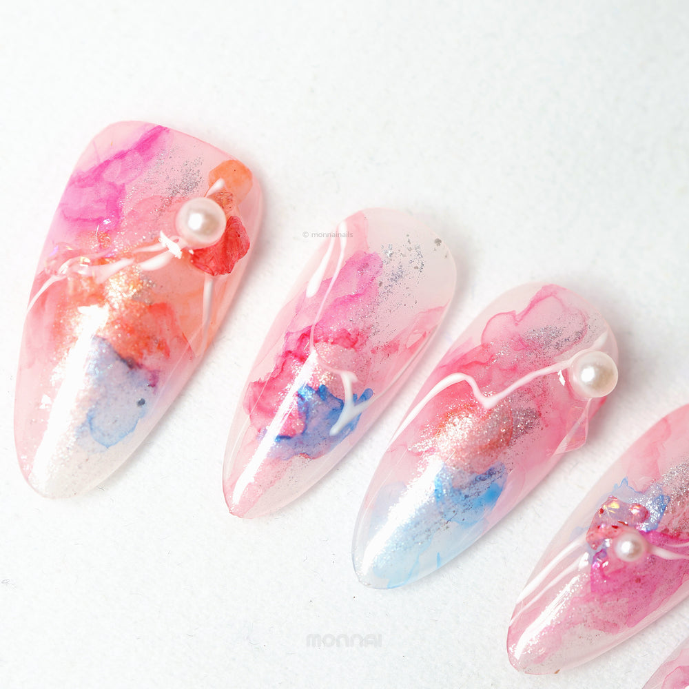 Whimsical Splash press-on nails laid out with pink and blue watercolor marble, silver shimmer, and pearl accents