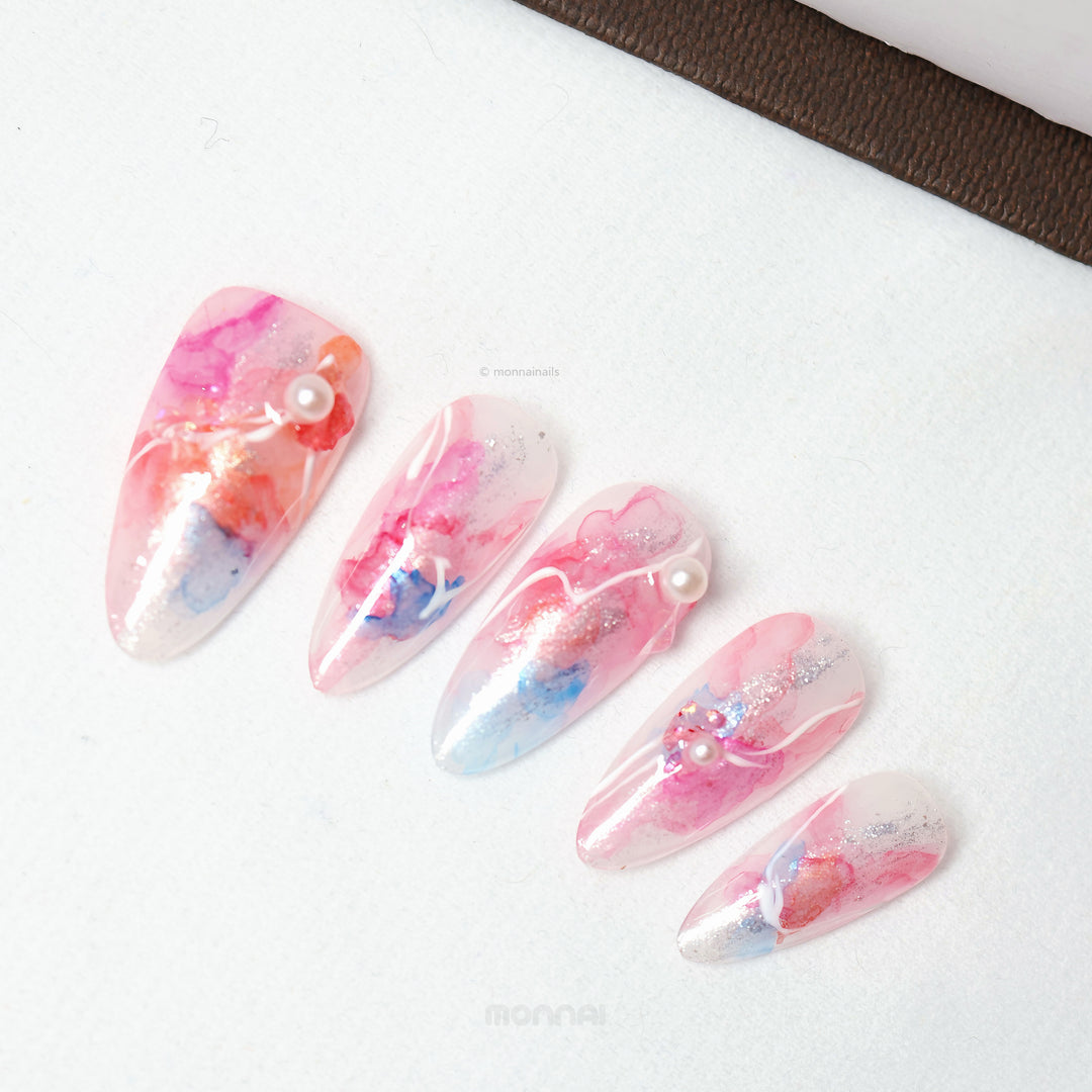Whimsical Splash ethereal press-on nails laid out with pink and blue watercolor marble, silver shimmer, pearl accents