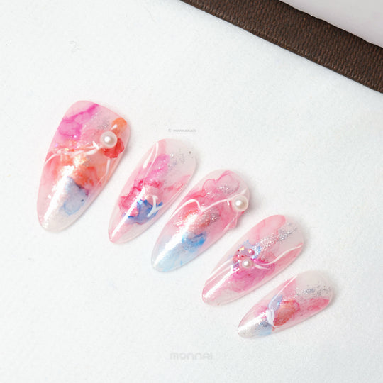 Whimsical Splash ethereal press-on nails laid out with pink and blue watercolor marble, silver shimmer, pearl accents