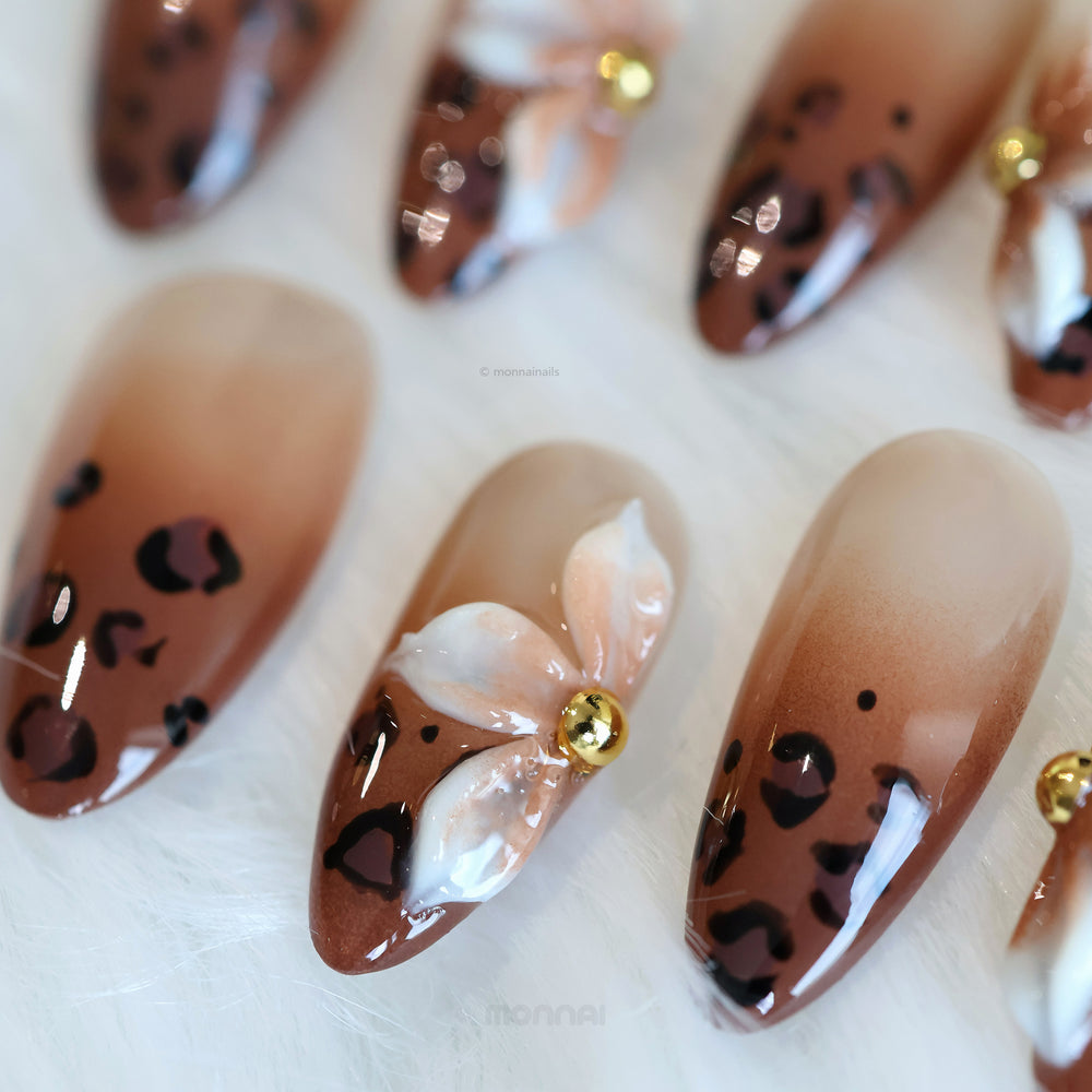 Wild Charm press-on nails in close-up, showing warm brown leopard print tips and a glossy floral accent with gold detail.