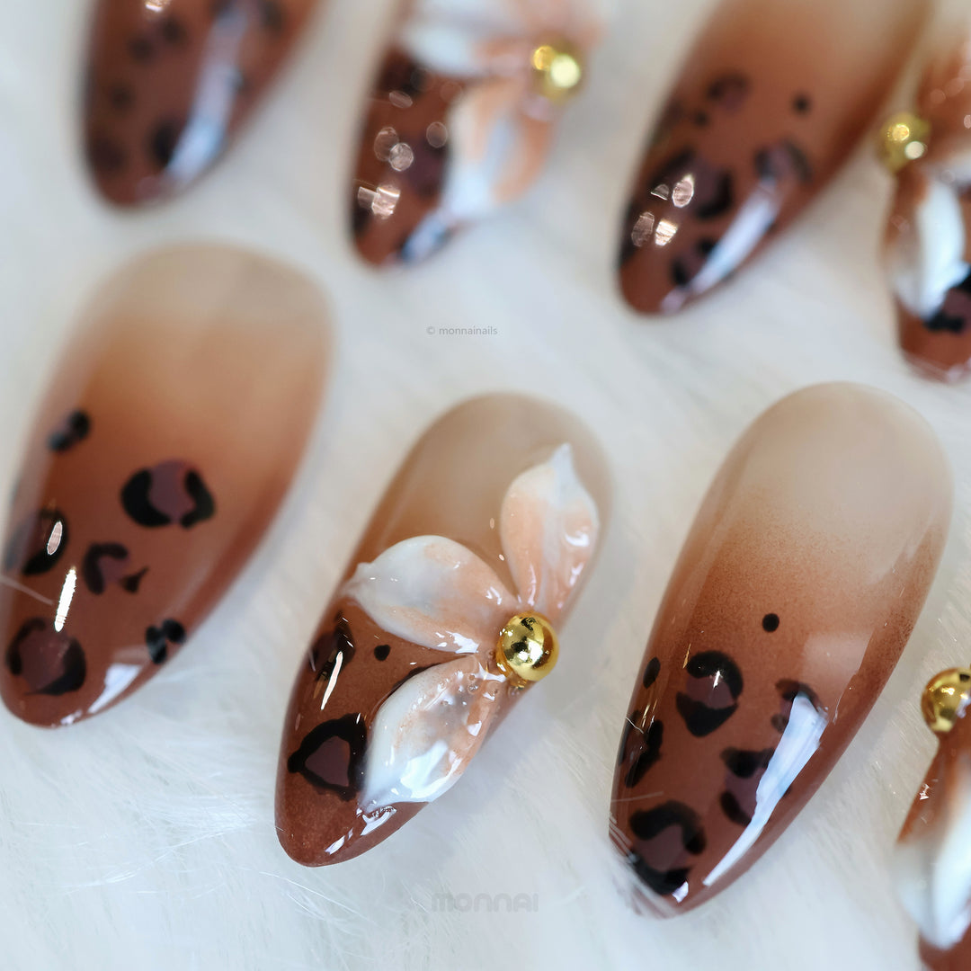 Wild Charm press-on nails in close-up, showing warm brown leopard print tips and a glossy floral accent with gold detail.