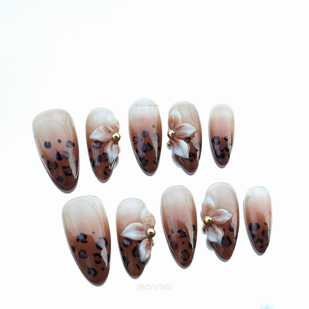 Wild Charm press-on nails laid out, with warm brown leopard print tips, white floral accents and gold details.