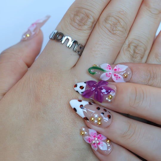 Wild Things press-on nails worn on hand with pink and plum 3D flowers, leopard-print details, and rhinestones