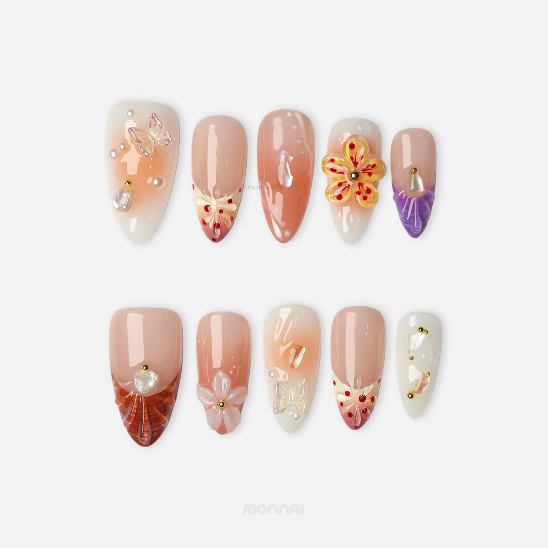 Winged Grace press-on nails shown laid out, with soft peach, sheer nude, butterfly and floral details, and pearl accents