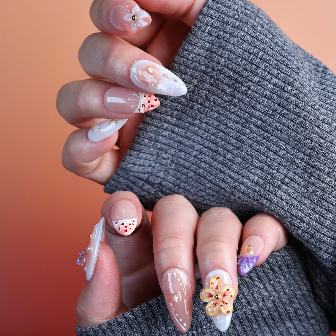 Winged Grace press-on nails on hands in soft peach and sheer nude tones with butterfly, floral and pearl accents