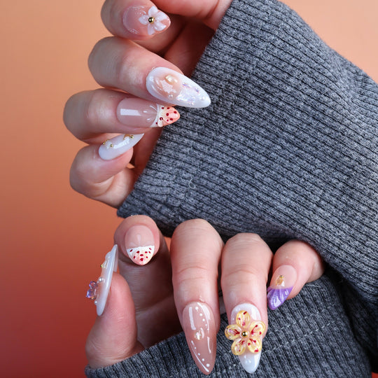 Winged Grace press-on nails on hands in soft peach and sheer nude tones with butterfly, floral and pearl accents
