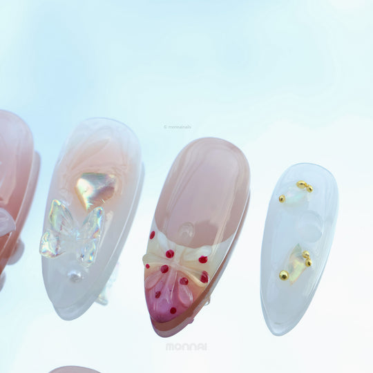 Winged Grace press-on nails laid out in close-up, with sheer nude tones, butterfly accents, and pearl details