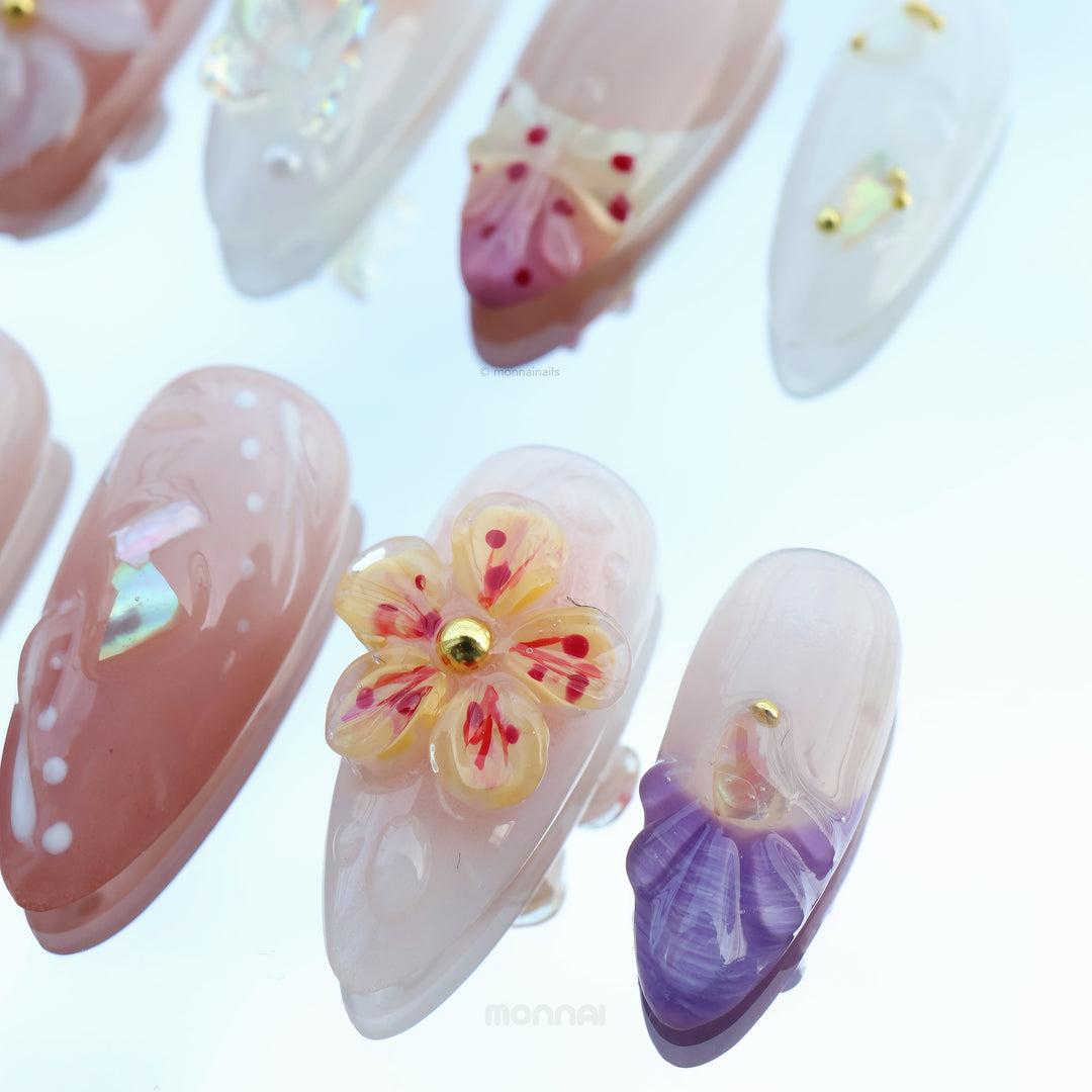 Winged Grace press-on nails shown close-up with soft peach, sheer nude, butterfly and floral details.