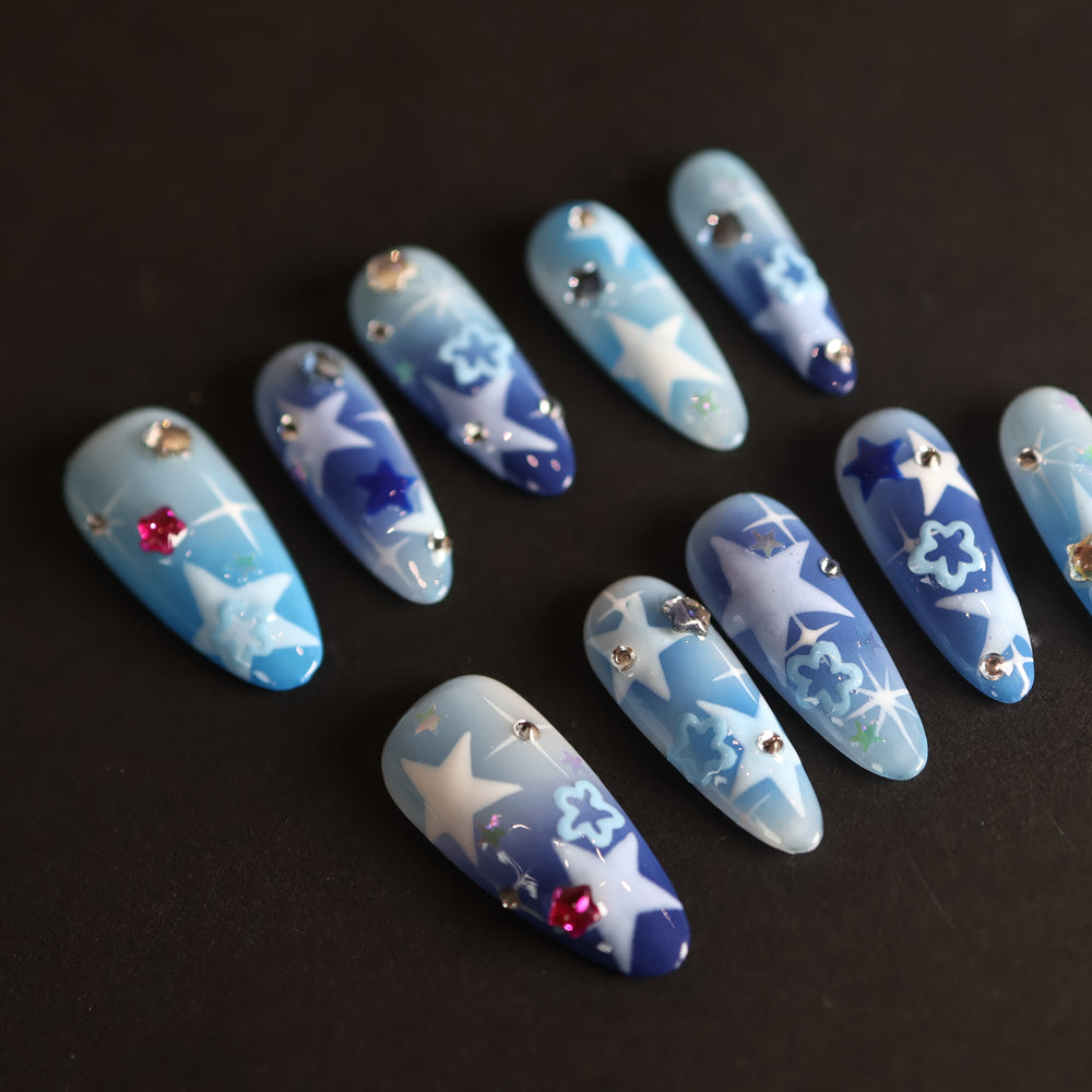 Wishing Jar press-on nails laid out with dreamy blue-to-navy star designs and scattered rhinestones