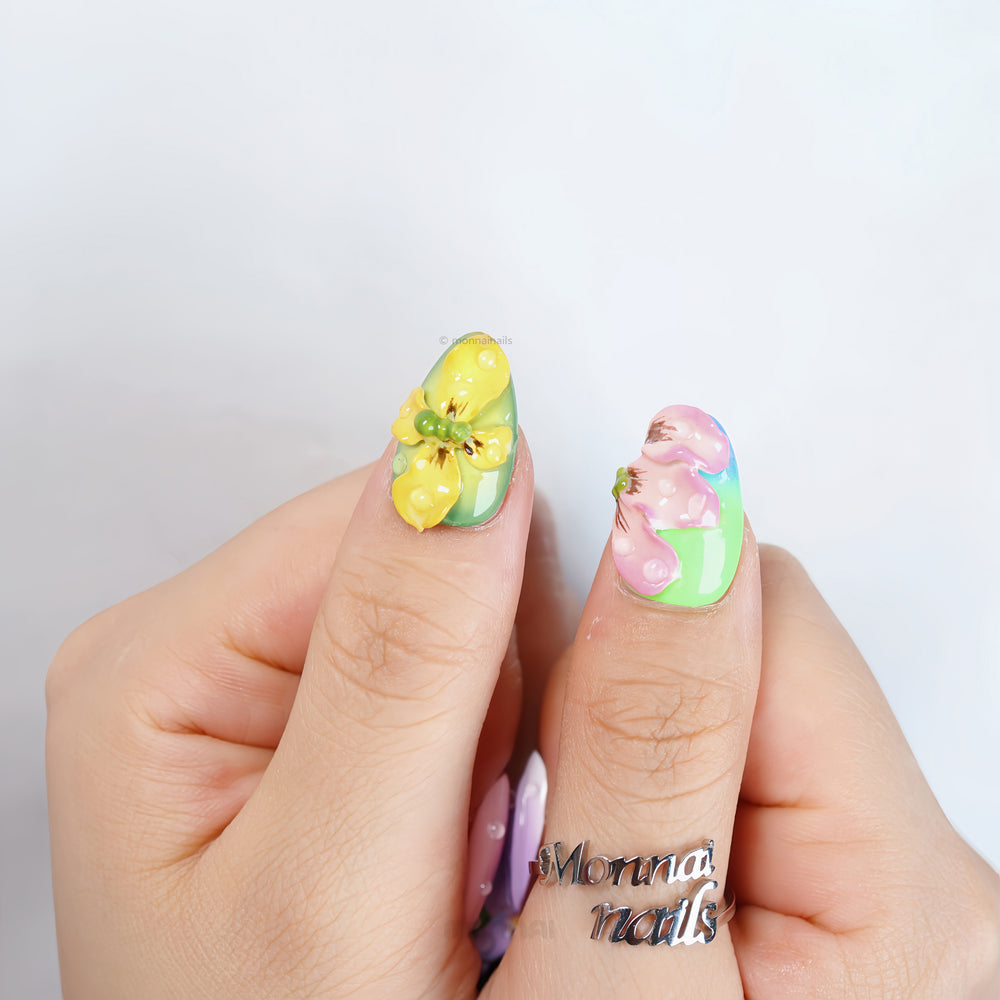 Wonderland press-on nails on hands with pastel floral 3D details, glossy water-drop accents, and gel-gloss finish