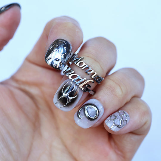X-Edge press-on nails worn on hand, monochrome cybercore and grunge design with 3D chrome lines and crackle textures.