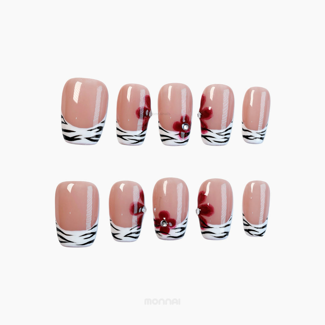 Zebra Blossom press-on nails with nude base, zebra French tips, and red floral accents shown laid out.