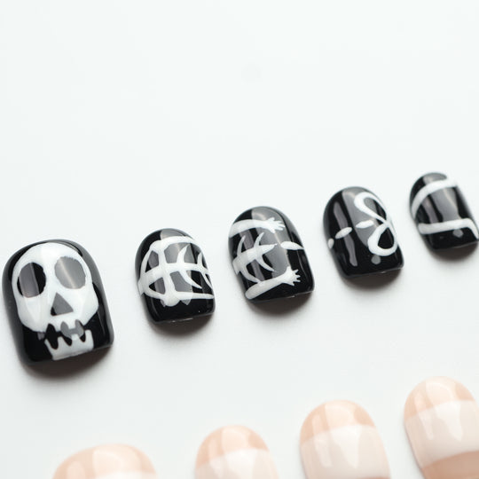Bone Party press on nails with black skull art, white skeletal details, and nude bandage stripes for spooky Halloween style