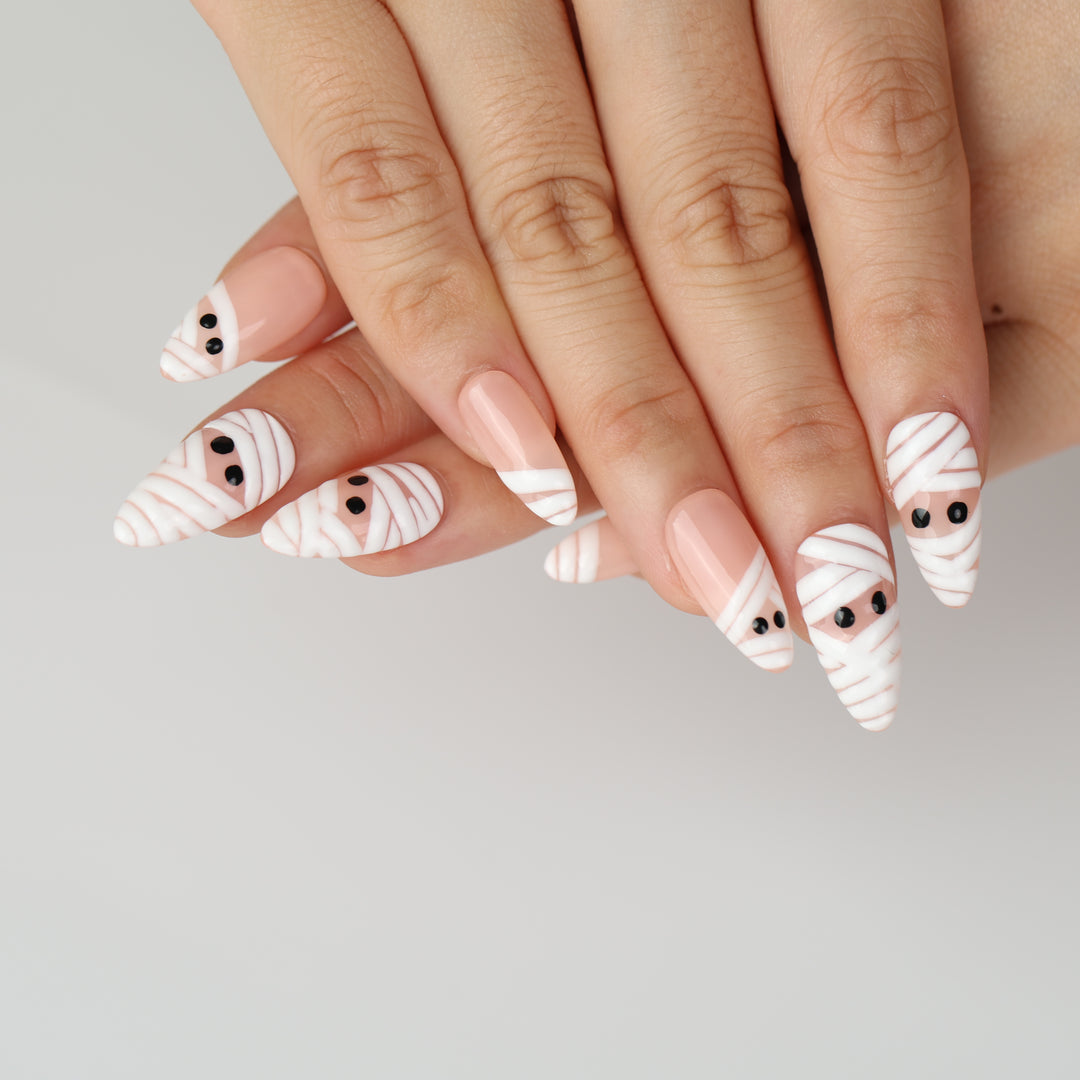Peekaboo Mummy press-on nails on hands with white bandage wraps, nude base, and black eyes