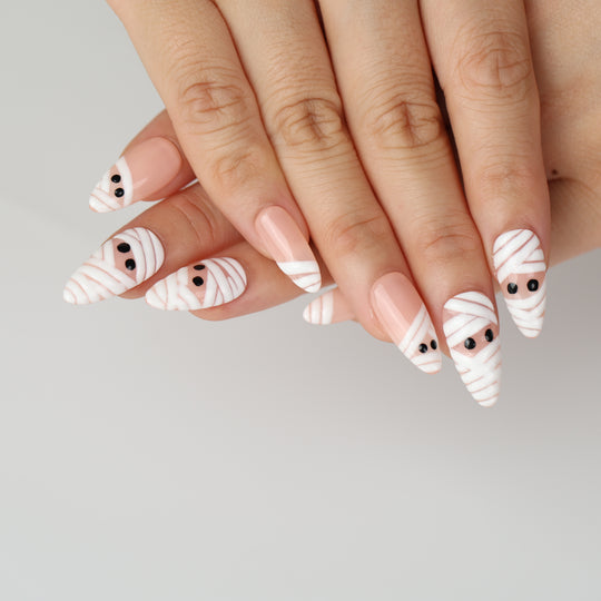 Peekaboo Mummy press-on nails on hands with white bandage wraps, nude base, and black eyes