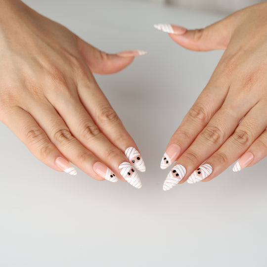 Peekaboo Mummy press-on nails on hands, white bandage stripes and black eyes on nude glossy nails