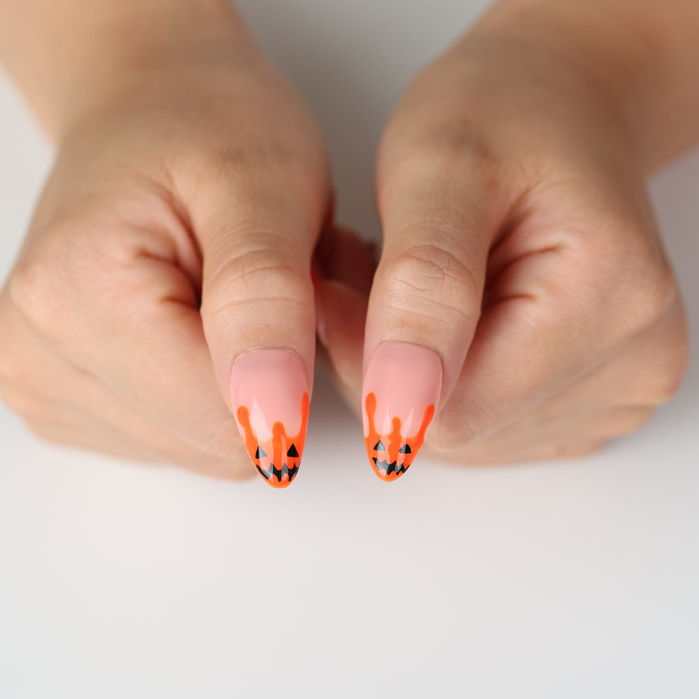 Pumpkin Drip press-on nails on hands with orange drip pumpkin faces and nude base