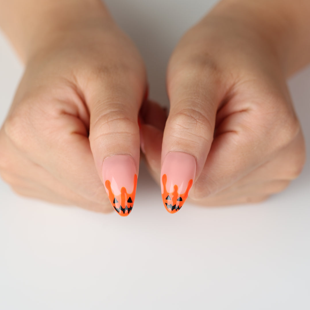 Pumpkin Drip press-on nails on hands with orange drip pumpkin faces and nude base