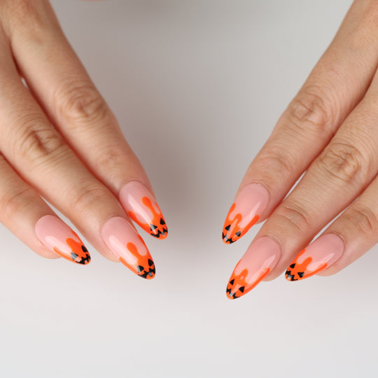 Pumpkin Drip press-on nails on hands with nude base, orange drip tips, and black jack-o&