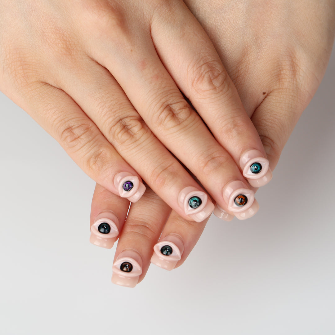 Spellbound Gaze press on nails with 3D eye details on a glossy peachy nude base