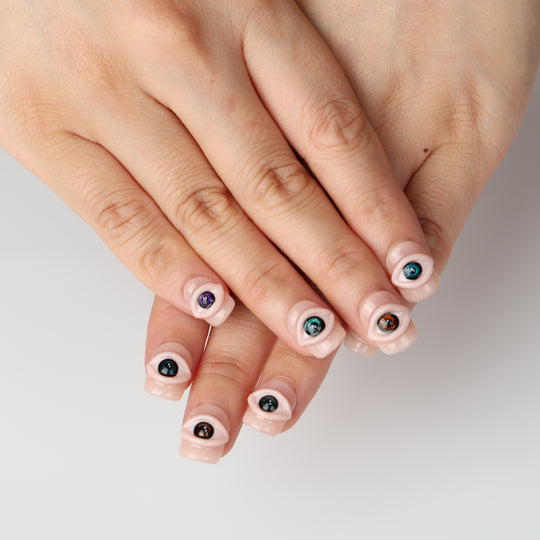 Spellbound Gaze press on nails with 3D eye details on a glossy peachy nude base
